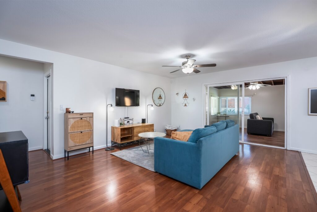 Living room interior of 2170 Montclair St in North Park featuring hardwood floors, a blue sectional sofa, and a wall-mounted TV.