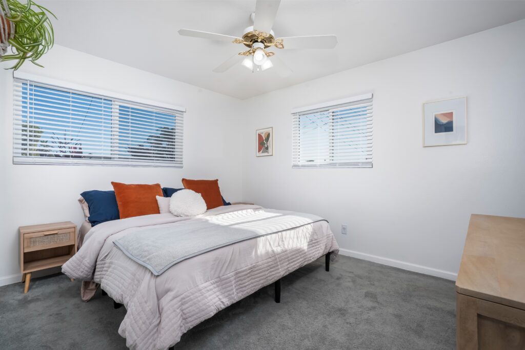 Sun-drenched primary bedroom at 2170 Montclair St in North Park featuring white walls, plush grey carpet, and large windows with Venetian blinds.