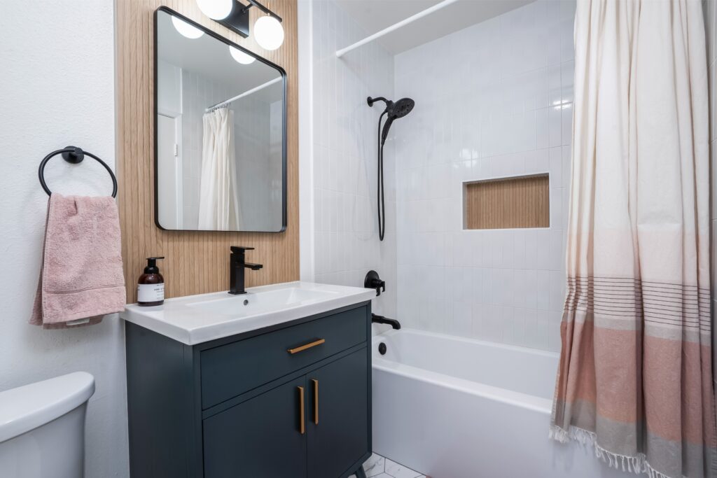 Newly remodeled bathroom at 2170 Montclair St North Park showcasing a dark navy vanity with gold hardware, white vertical tile shower, and wood-paneled accent wall.