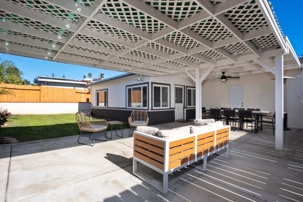 Backyard lounge area at 2170 Montclair St North Park home for sale, featuring a modern sofa under a weather-protected pergola overlooking a lush lawn and premium turf.
