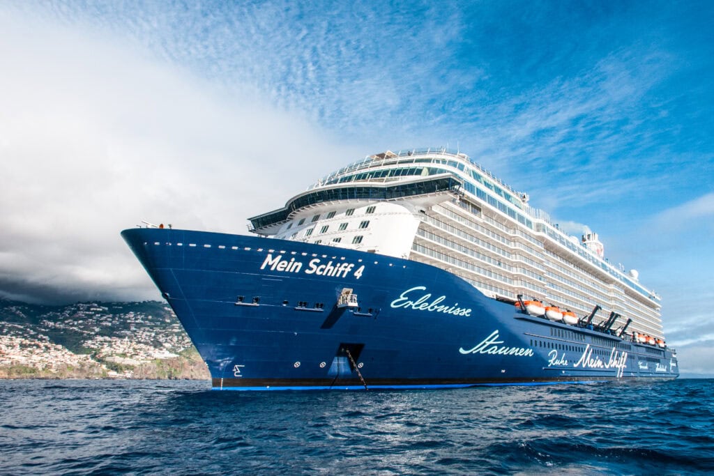 meinschiff4 aussenansicht - Michis Kreuzfahrten ein großes kreuzfahrtschiff mit der aufschrift'Mein Schiff 4' auf dem Wasser, umgeben von einem klaren Himmel und einer Küstenlandschaft im Hintergrund.