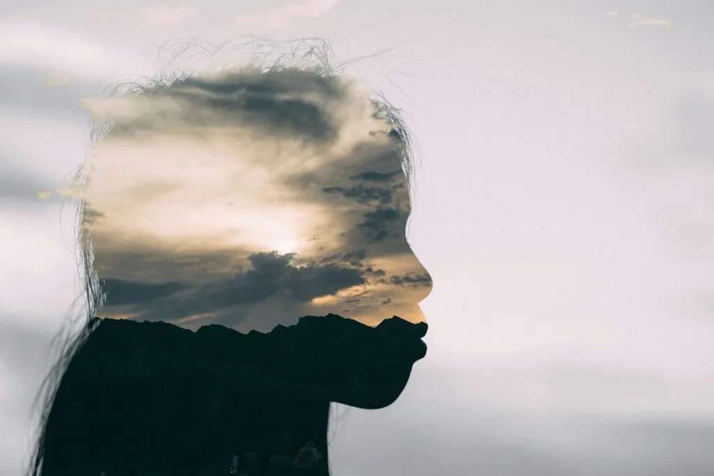 Mixed media photograph of a woman's profile from the neck up. The edited upper portion of her profile features a cloudy sky.