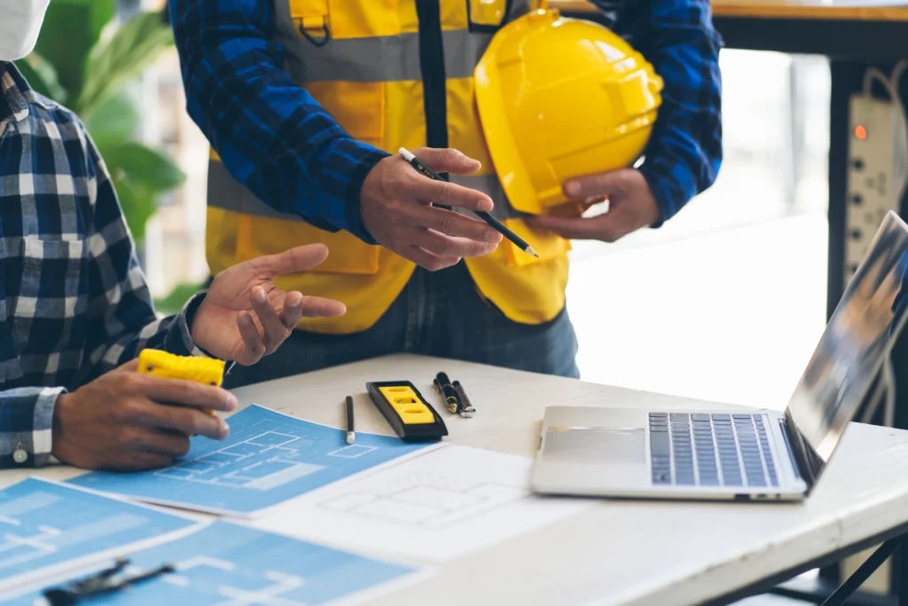 Engineers analyzing building blueprints with laptop and digital tools on construction site