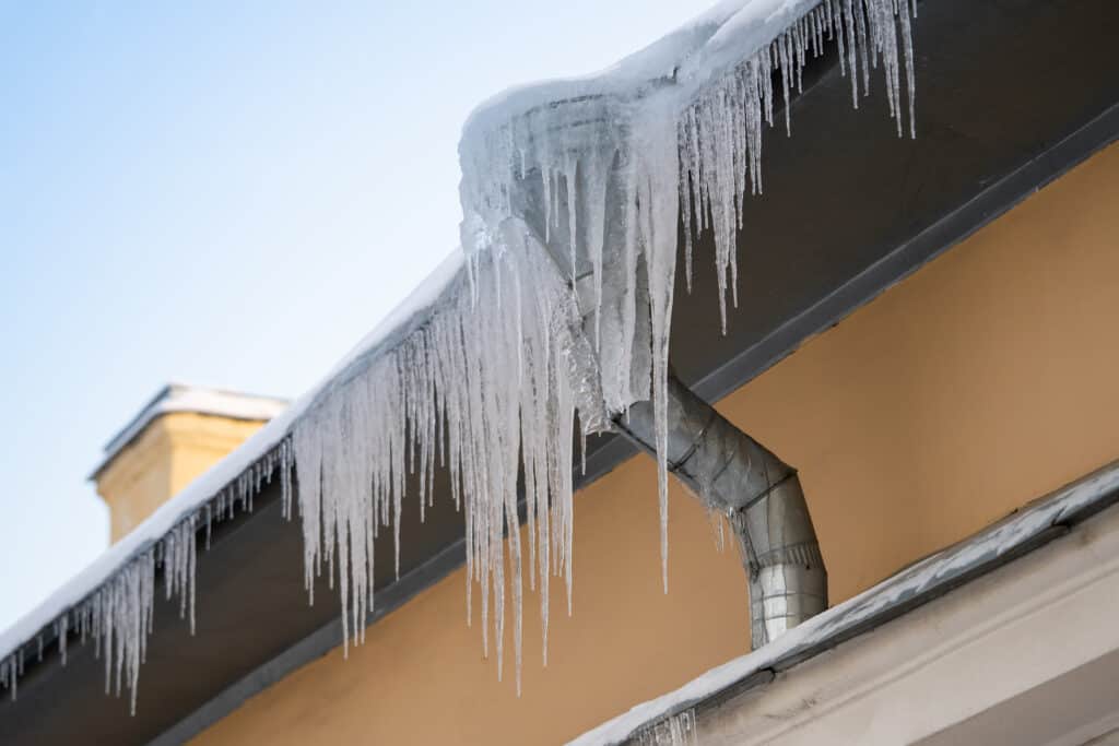 Frozen ice. frozen icicles dangerously hanging from building edge on cold winter day, dangerous ice formation on metal house roof during bright sunny, but sub-freezing weather outside