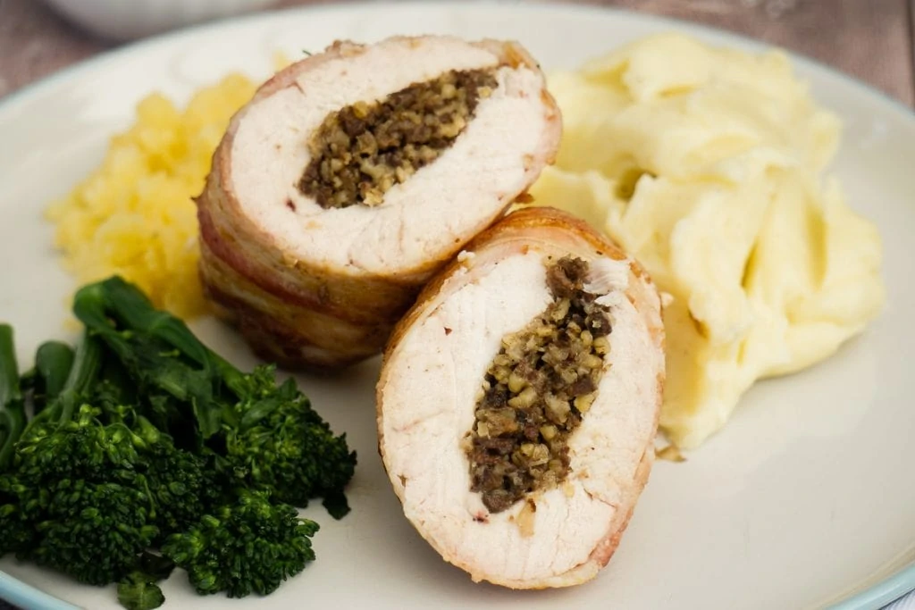 Chicken Balmoral - Chicken stuffed with haggis wrapped in bacon on a plate with vegetables and whisky sauce