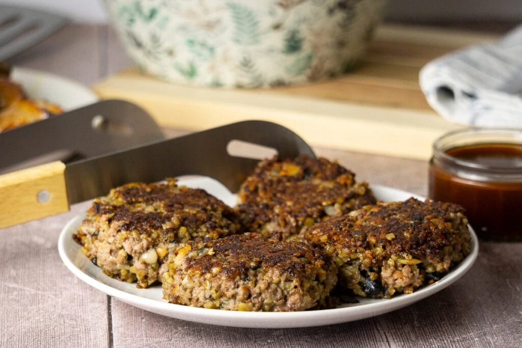 Haggis Burgers on a plate with tongs and barbeque sauce in the background