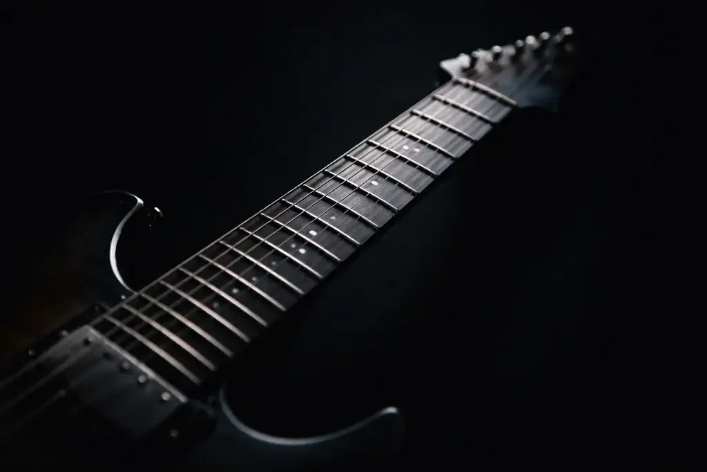 Close-up of an electric guitar neck and strings emerging from darkness, symbolizing timeless guitar songs and immortal riffs