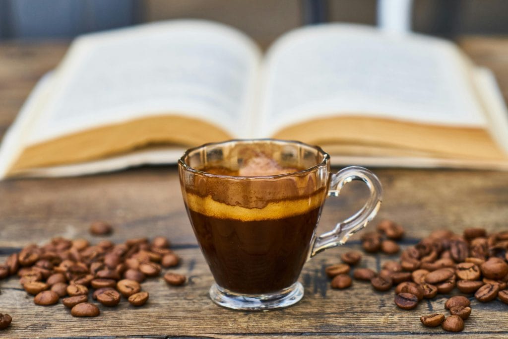a single espresso on a table with coffee beans sitting in front of an open book