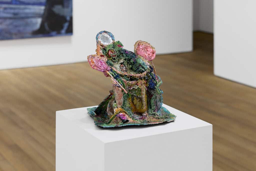 A colorful, abstract ceramic sculpture with glittery textures and iridescent sections sits on a white pedestal in Ginny on Frederick’s Frieze 2025 presentation, part of Crude Hints Towards curated by Charlotte Edey.