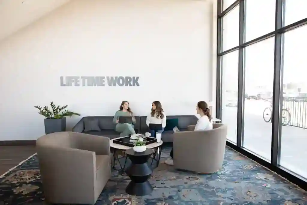 Modern Raleigh coworking lounge with comfortable seating, large windows, and professionals collaborating in a bright shared workspace within a residential community.