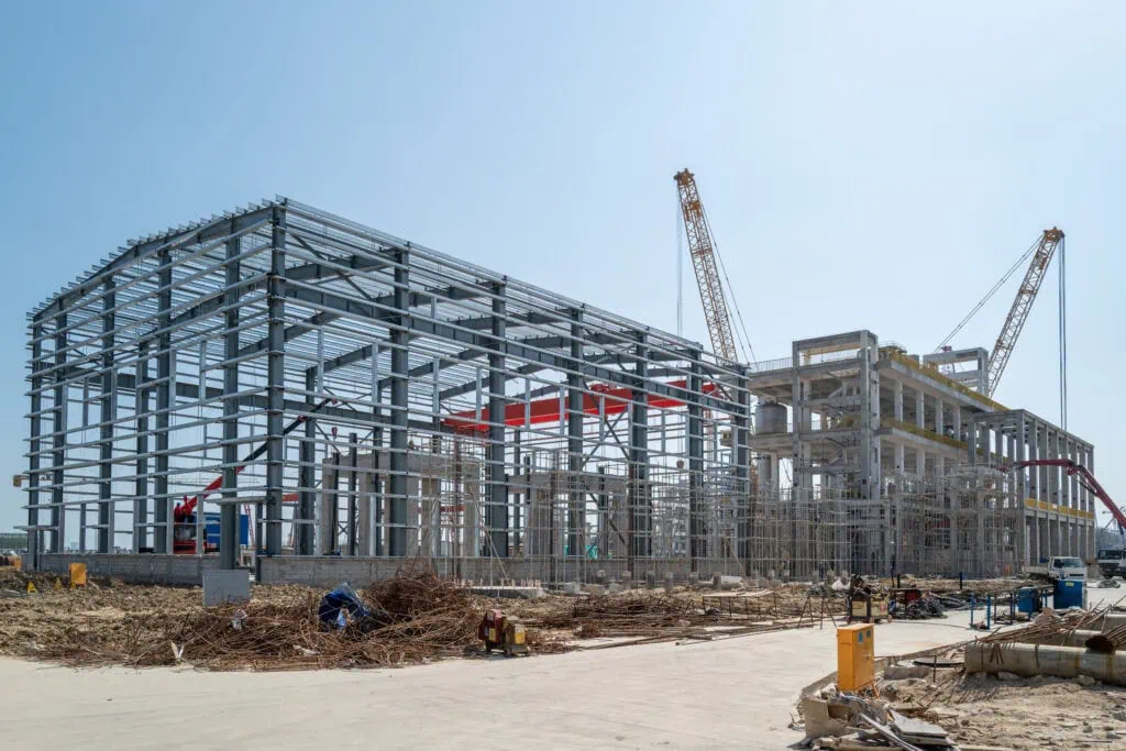 A steel building under construction with workers wearing safety gear and Canadian flags visible in the background.