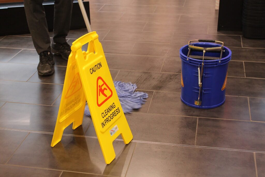 yellow caution cleaning in progress signage on the floor, along with blue bucket and mop and cleaner mopping the floor of Sydney's retail store