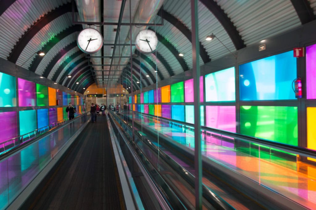Colorful windows lining both sides of escalator at inside an airport.