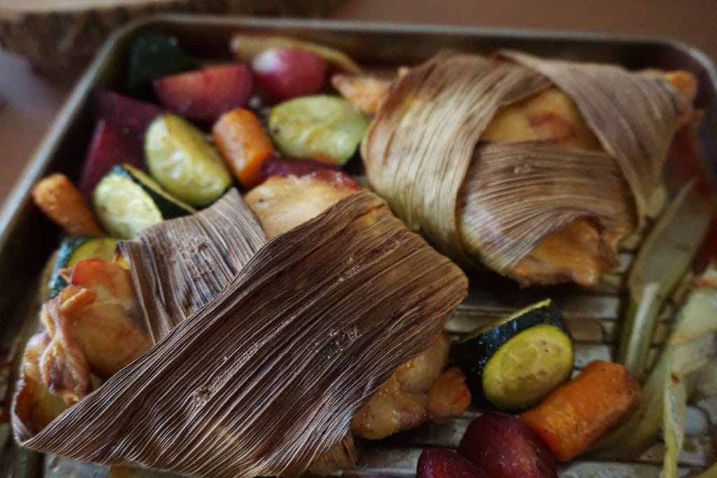 Corn husk-wrapped chicken and roasted veggies at an low angle