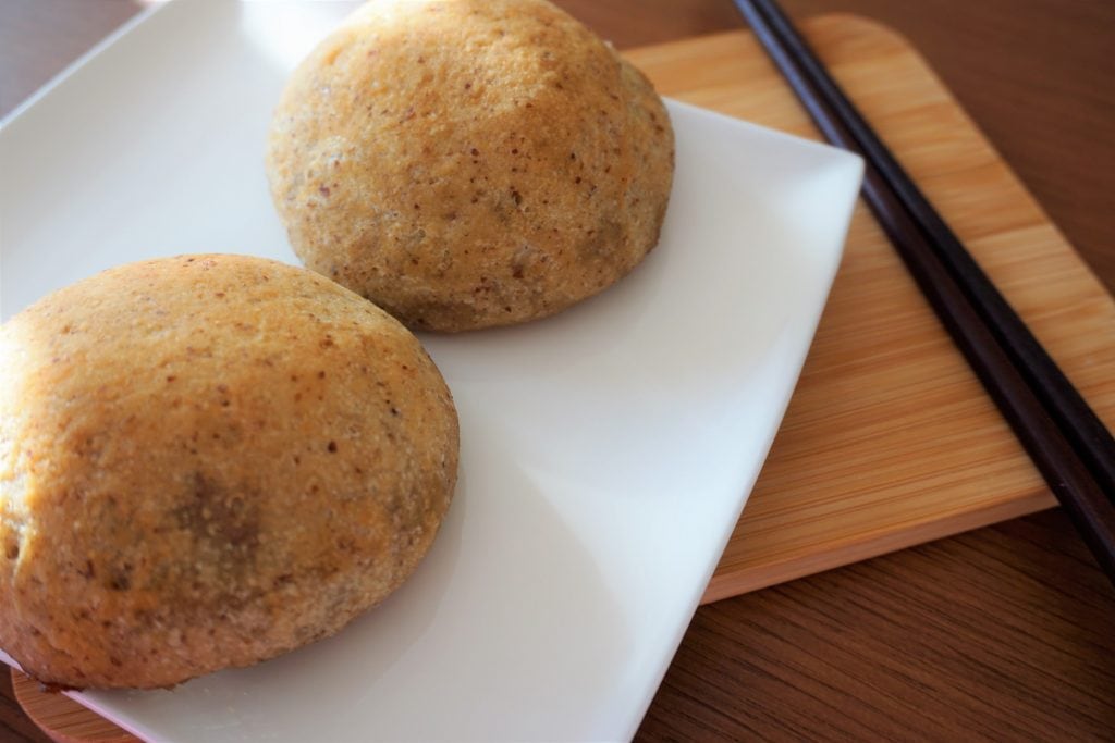 two baked bbq pork buns on a square plate with a pair of chopsticks on the side