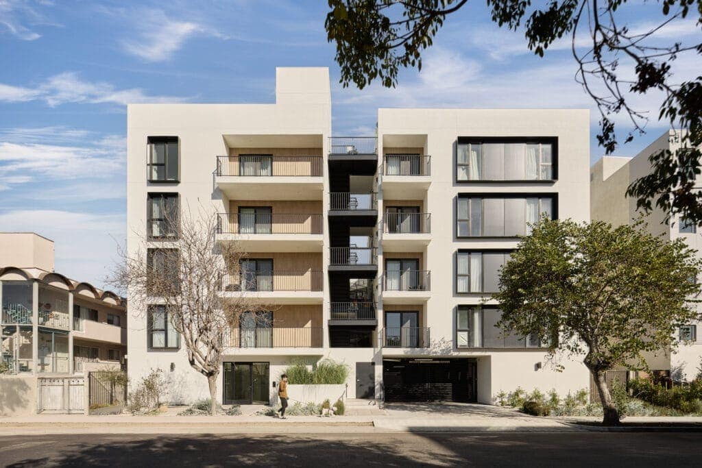 Modern multi-story residential building with a minimalist design, white stucco facade, and black window frames.