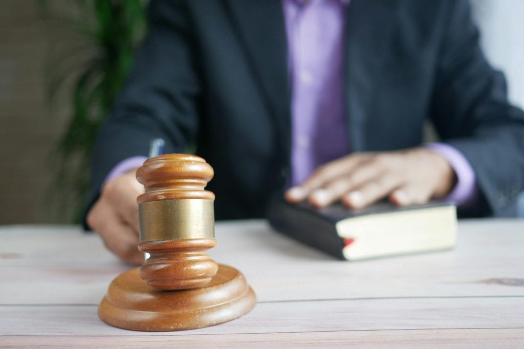 Male in suit with hand on a book and holding a gavel