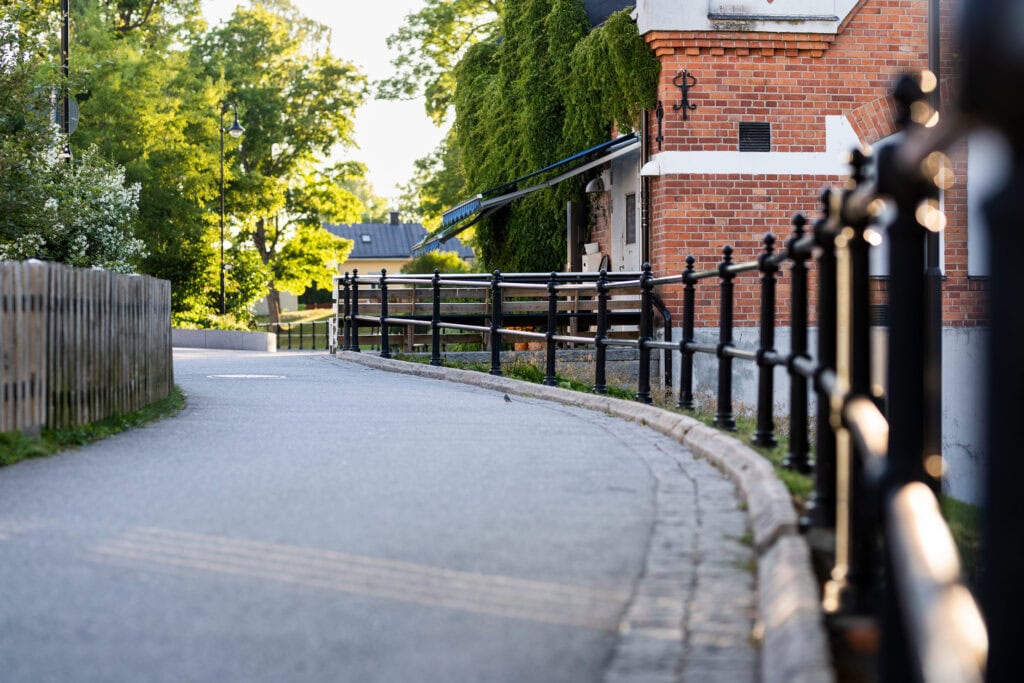 Gångväg med staket vid en tegelbyggnad och gröna träd i bakgrunden.