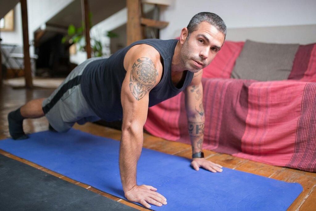 a tattoed man doing push up on a yoga mat