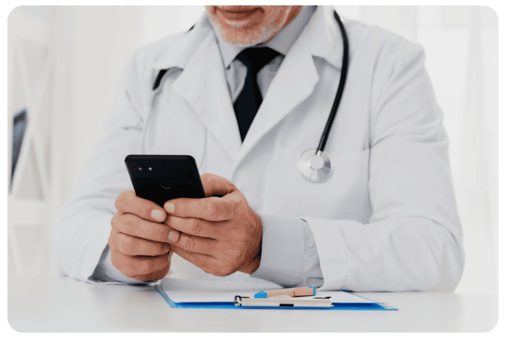 A doctor using a mobile phone to access mHealth apps with a clipboard and stethoscope on the desk. Mobile Healthcare Apps.