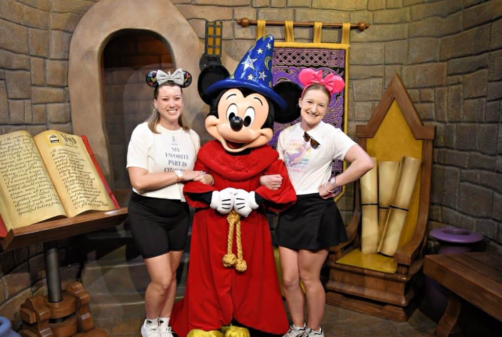 Mickey Mouse with two women at Disney-themed indoor attraction.