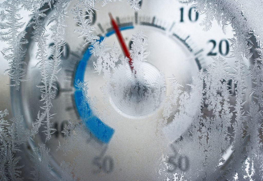 En närbild av en termometer delvis täckt av frost. Röda och blå markeringar syns på termometern.