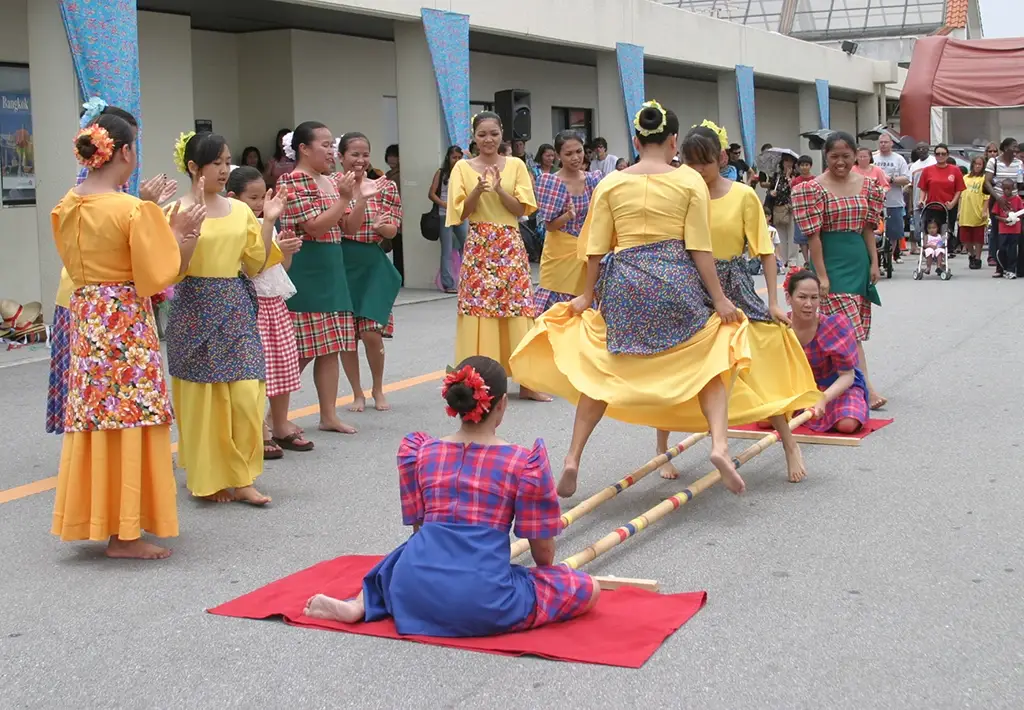 Tinikling dancers leaping between bamboo poles in traditional Filipino clothing.
