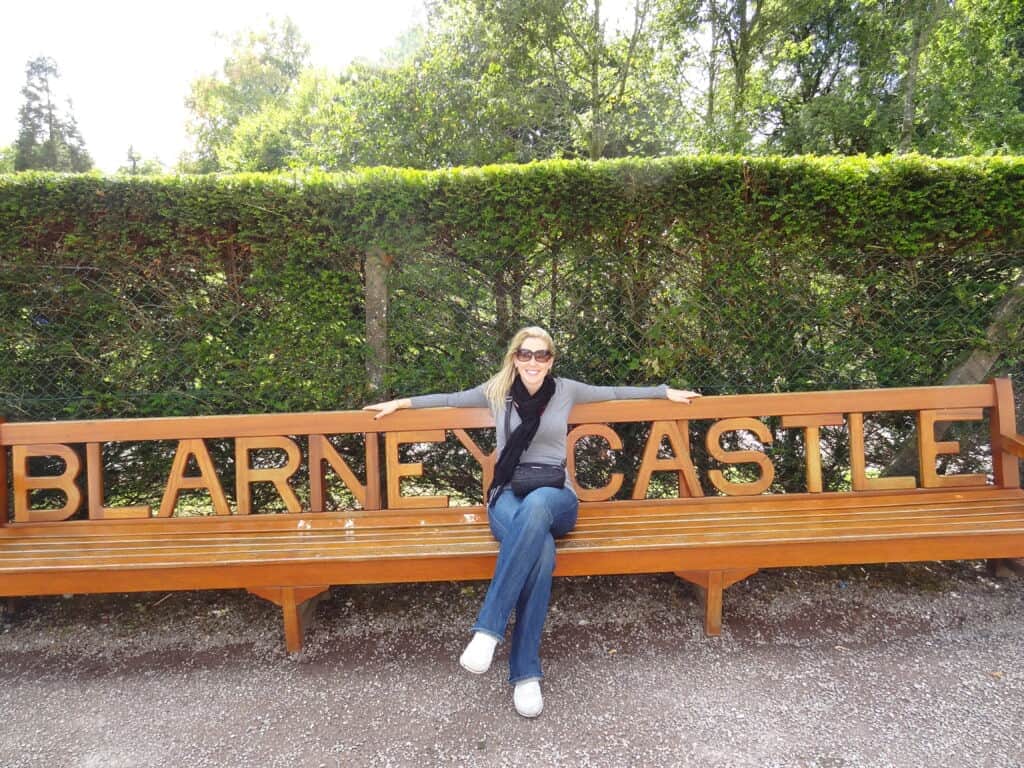 Woman sitting on a bench at Blarney Castle in Ireland with arms outstretched.