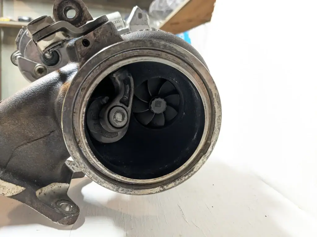 Turbine-side view of an IS20 turbocharger. The turbine wheel and wastegate flapper are clearly visible inside the housing, with typical carbon buildup. Useful for illustrating wastegate movement versus shaft play during inspection.
