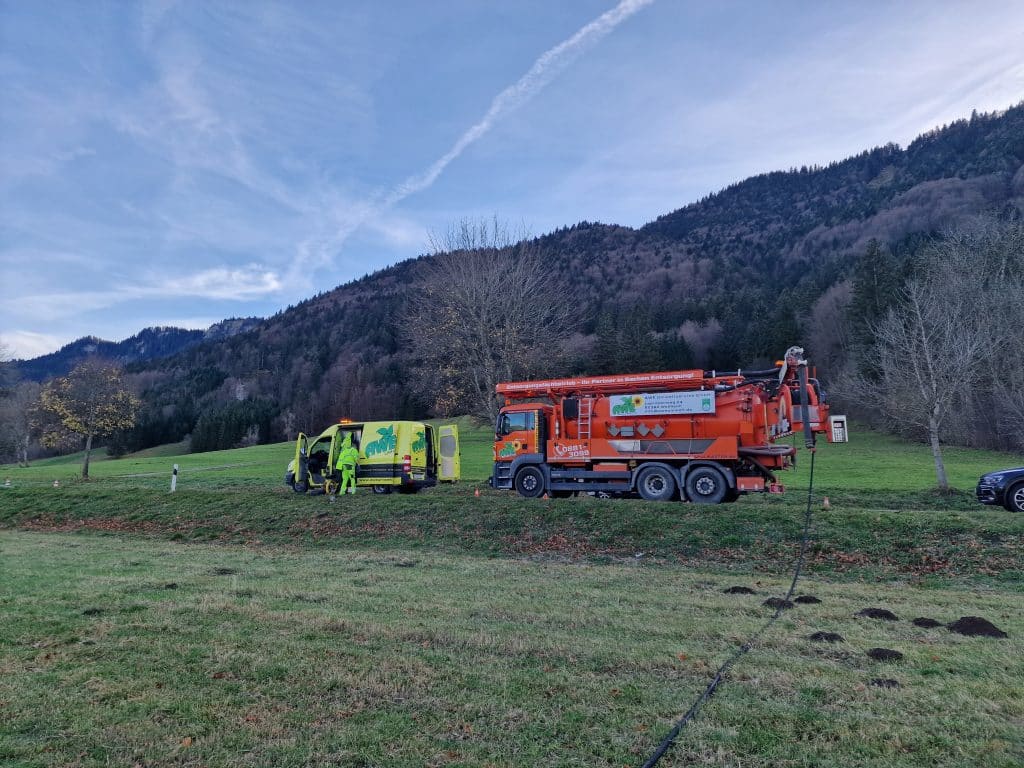 „Kanalspülfahrzeug und Kamerainspektionsfahrzeug vor bewaldeter Bergkulisse – Spülschlauch am Nachmittag ausgelegt“