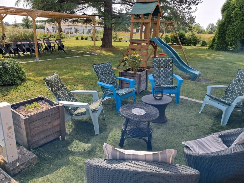 Terrasse extérieure avec chaises bleues, table basse, bac à plantes et aire de jeux en bois