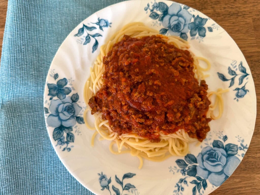 How to Make Spaghetti Sauce Thicker. Plate of spaghetti topped with rich tomato sauce, served on a white dish with blue flowers.
