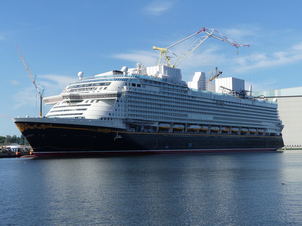 das neue kreuzfahrtschiff disney adventure wird gerade im hafen getestet, umgeben von wasser und kranen.