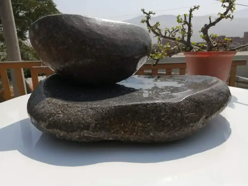 Persona limpiando un batán de piedra con una escobilla y agua natural