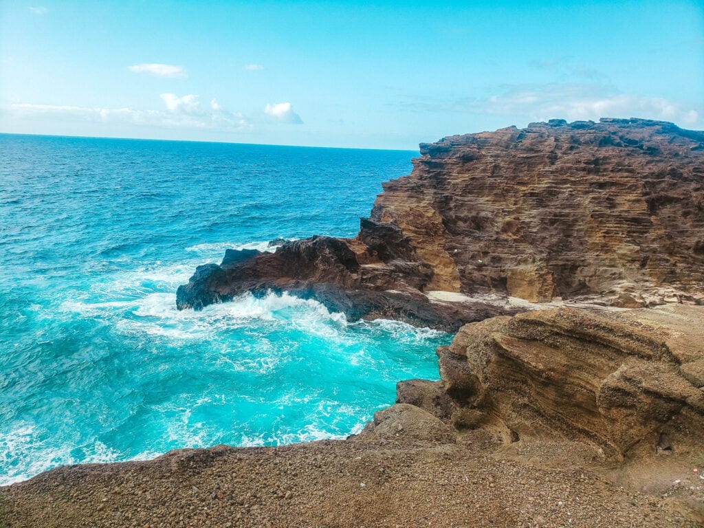 View of rugged lava rock cliffs and bright turquoise waves crashing against the shoreline near the Halona Blowhole Lookout on Oʻahu’s southeastern coast.