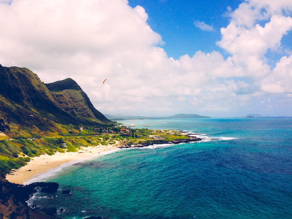 View of Waimanalo Beach on Oʻahu, Hawaiʻi, featuring turquoise waters, a wide stretch of soft white sand, and lush green mountains under a partly cloudy sky.