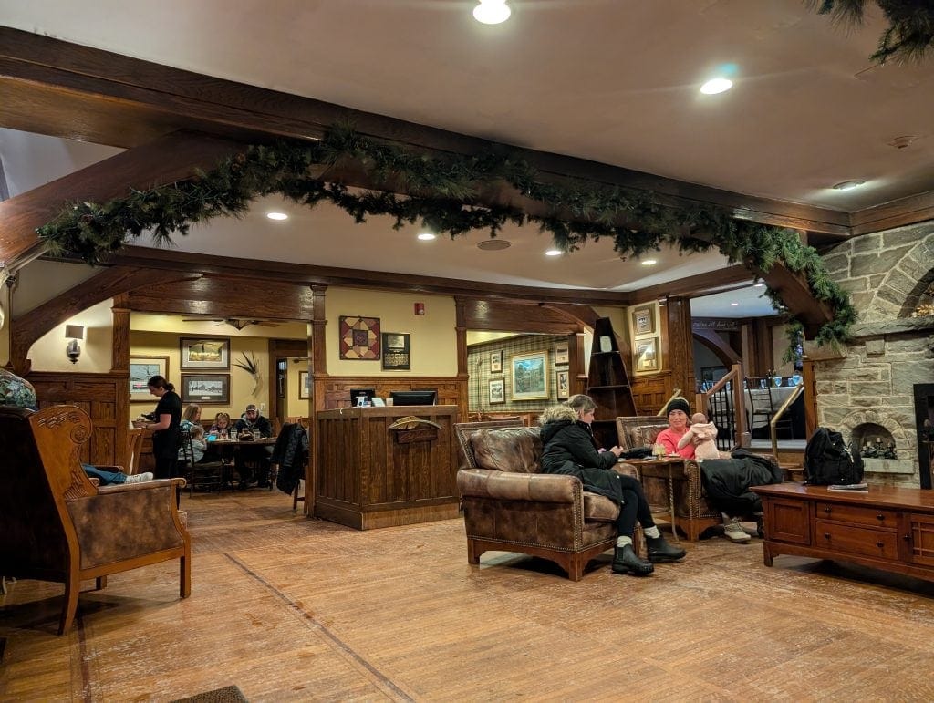 Interior of Timberlake's Restaurant at Chetola Resort, featuring warm wooden beams decorated with garland, a stone fireplace, leather seating, and guests enjoying meals and conversations in a cozy atmosphere.