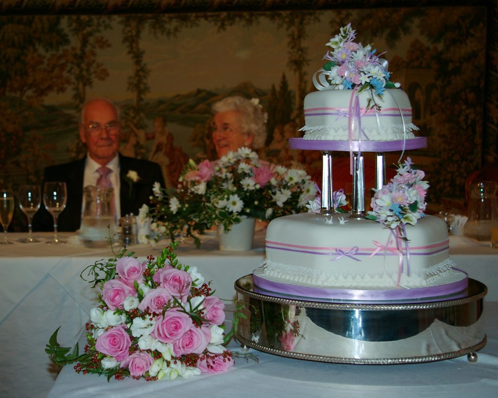 Elegant two-tier wedding cake with floral accents in front of smiling couple — part of EJC Photography’s timeless, heartfelt wedding coverage across Hampshire & Sussex