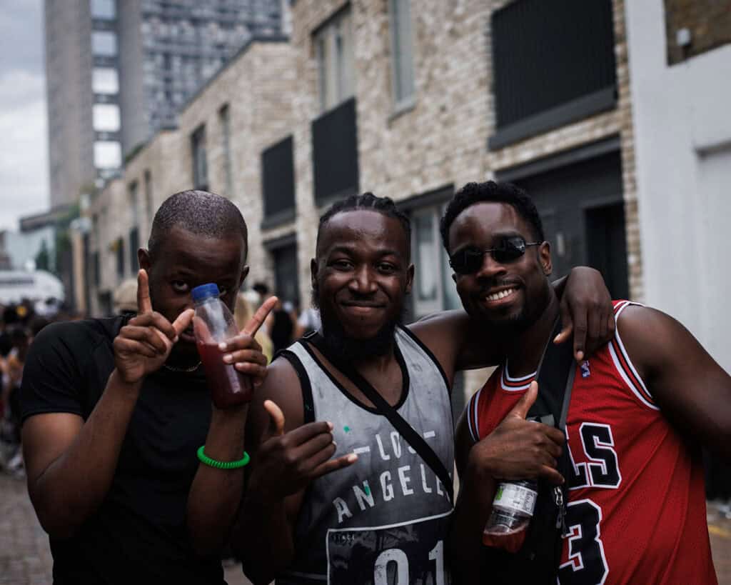 Three men smiling and holding drinks while celebrating Notting Hill Carnival.