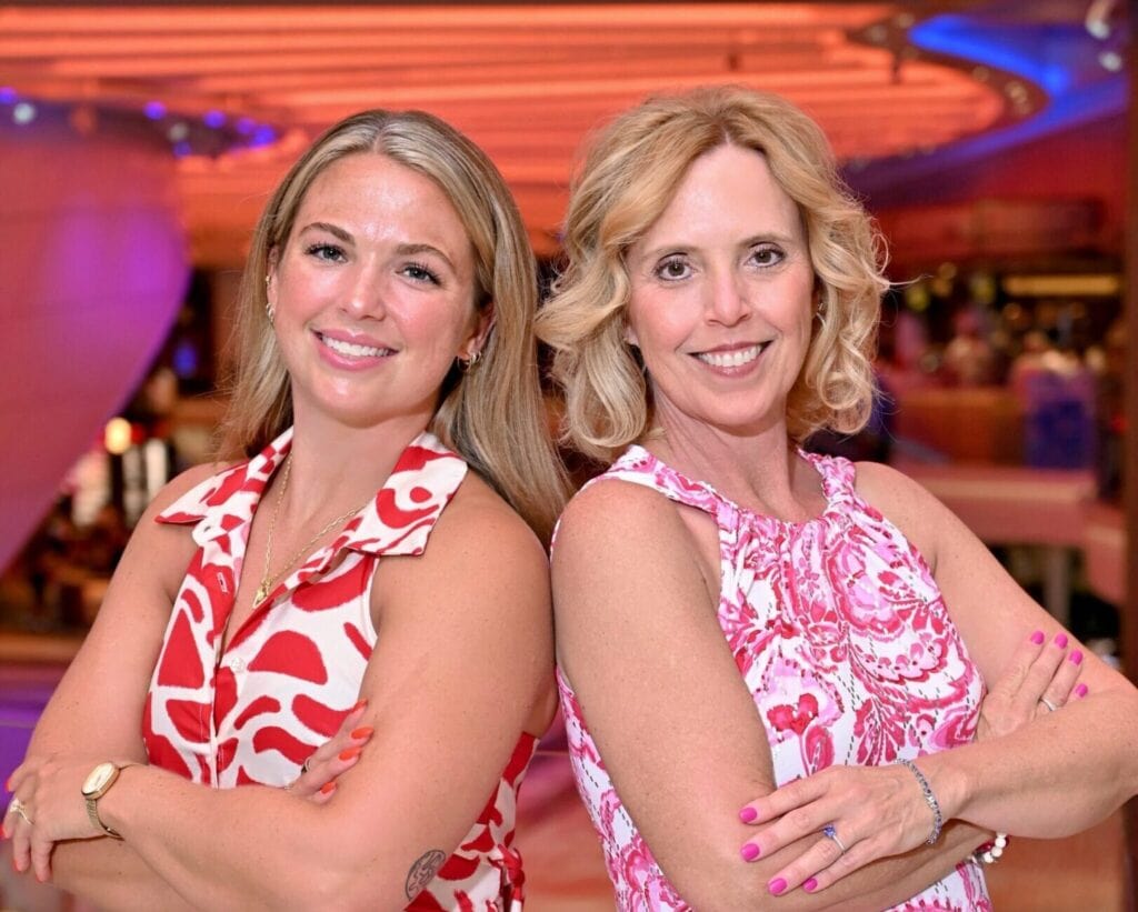 Mother-daughter duo on cruise ship atrium with vibrant lighting.