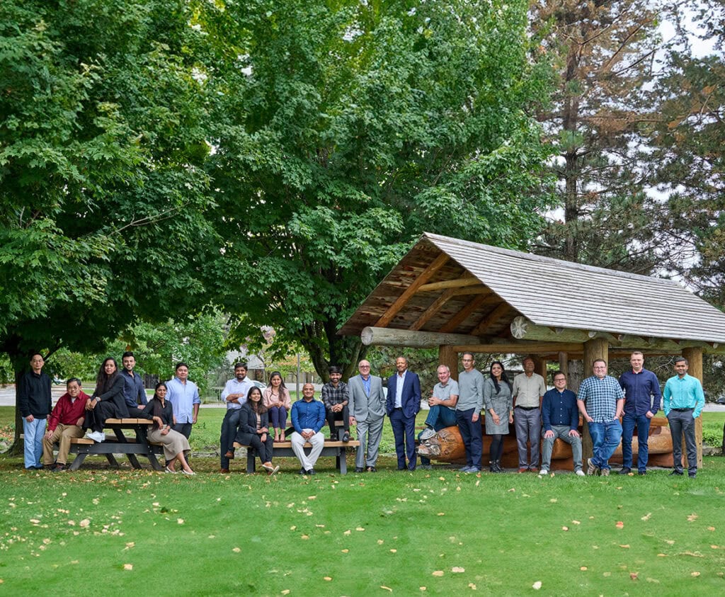 Team photo of Core Migration, outdoors, featuring a diverse group against a backdrop of trees and a wooden structure.
