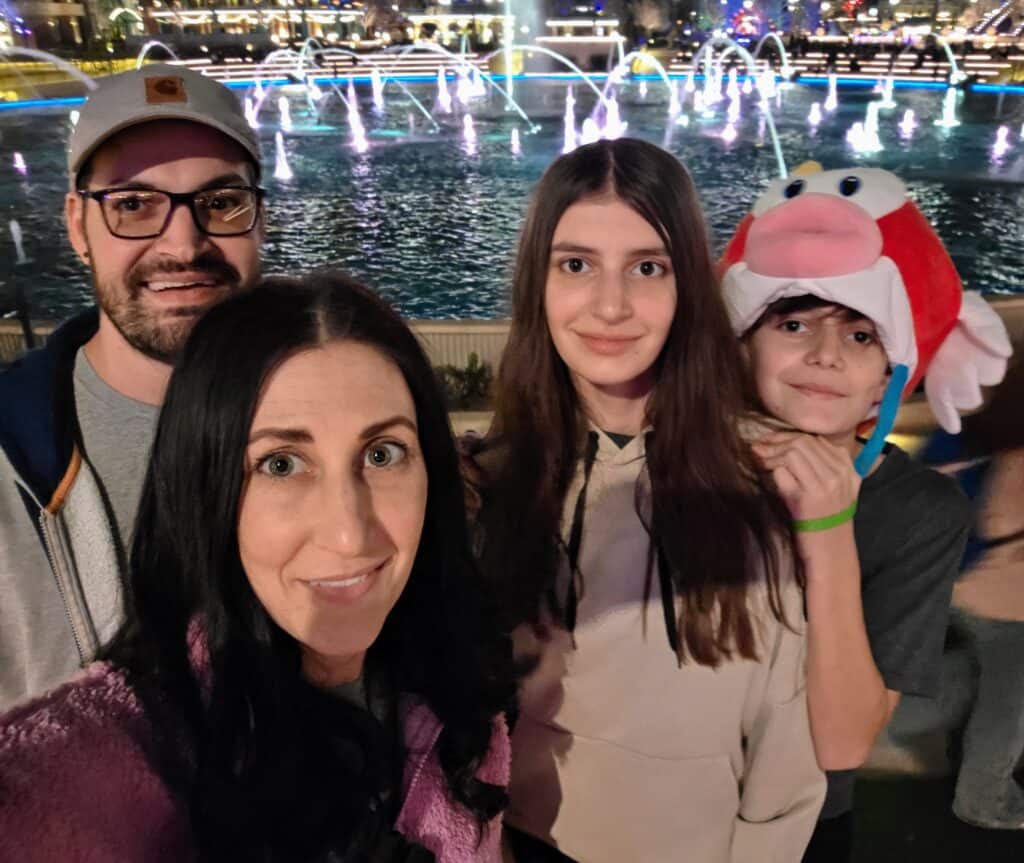 Family at fountain show with colorful water jets at night.