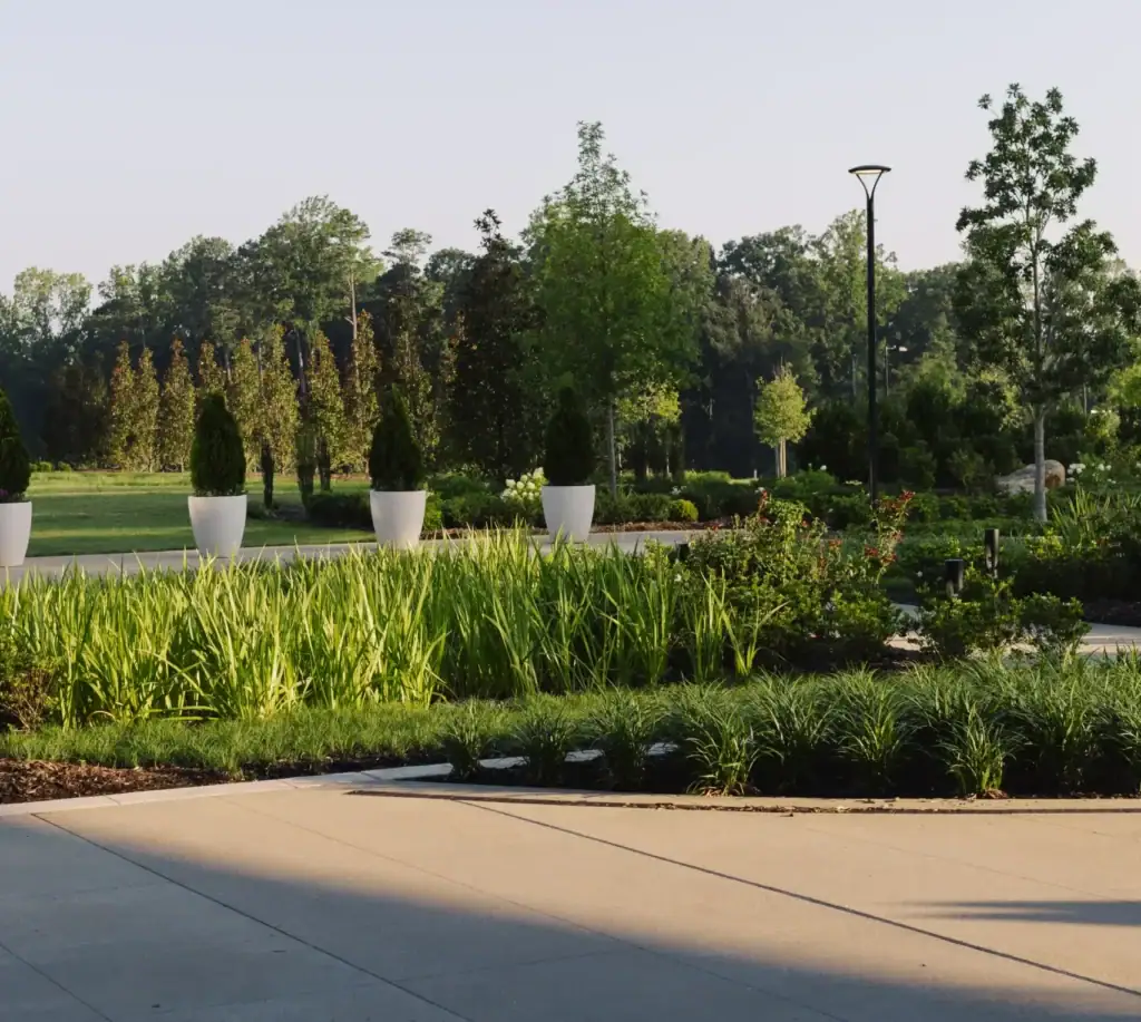 A beautifully landscaped Raleigh office building featuring manicured gardens, ornamental grasses, walking paths, and decorative planters under warm morning light.