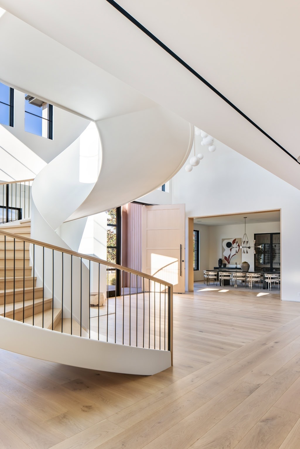 Sleek contemporary staircase with smooth white balustrade and wooden handrail, illuminated by natural light.