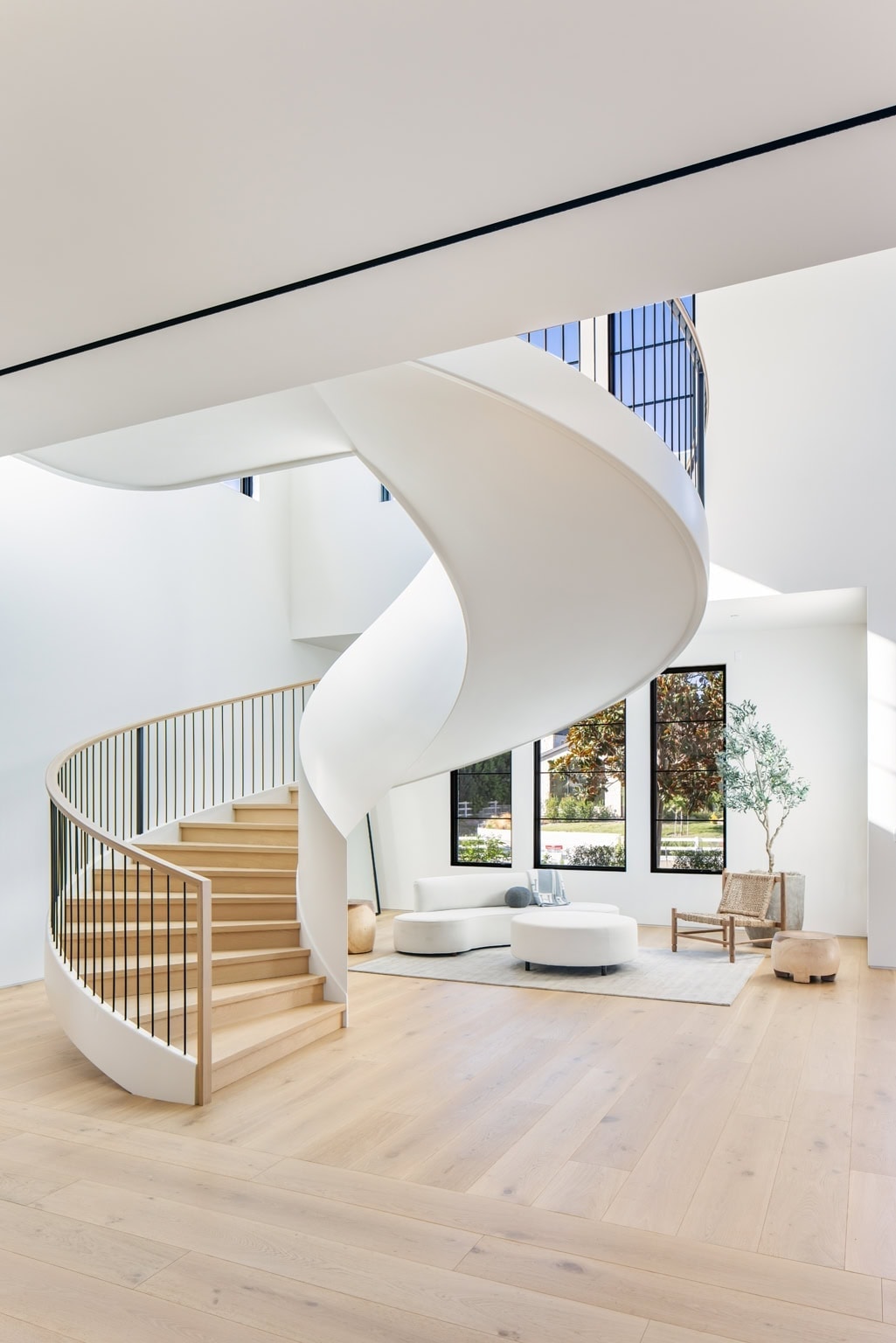Spiral staircase with wooden steps and white curved balustrade, modern minimalist living room with large windows.