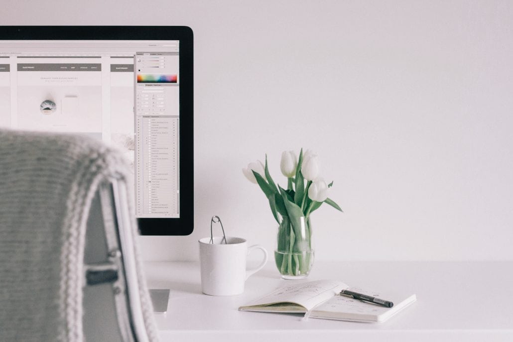 A desk with a computer and a vase of flowers.