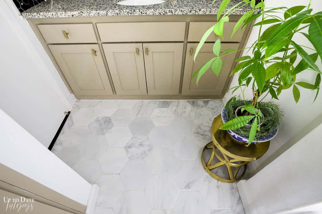 A bird's eye view of bathroom vanity white marble hexagon floor, gold stand with plant, and grey taupe cabinets.