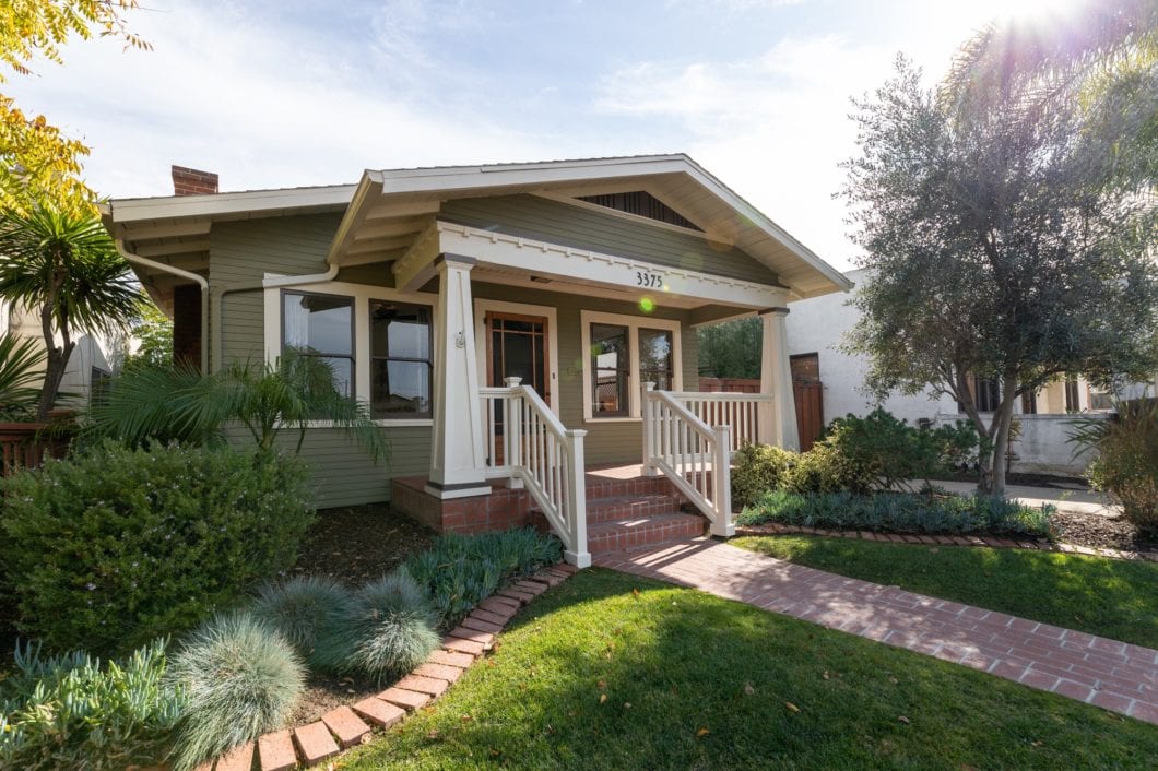 Charming Craftsman bungalow in Altadena, in North Park featuring an olive green exterior, white tapered columns on a front porch, and a manicured lawn with a brick pathway.