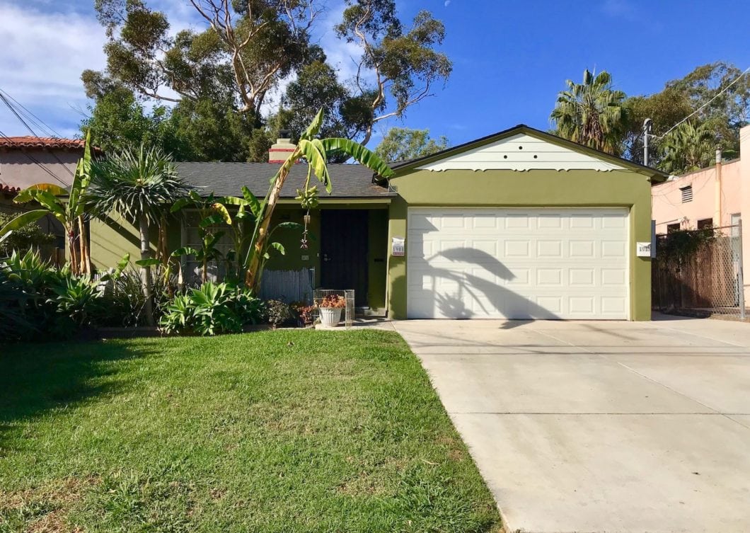 Vibrant olive-green duplex at 1908-10 31st Street in South Park featuring a two-car garage, lush tropical landscaping with banana trees, and a wide concrete driveway under a clear blue sky.