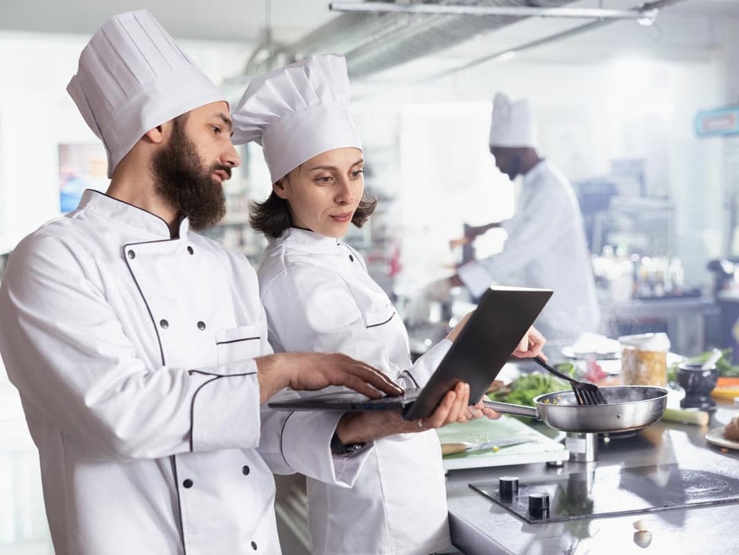 Zwei K&ouml;che planen die Warenwirtschaft mit dem Necta Group System. Sie optimieren Bestellprozesse in einer gro&szlig;en Edelstahl-Profi-Restaurantk&uuml;che.